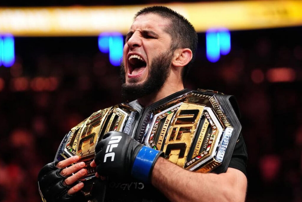 Islam Makhachev roars while holding two championship belts after a UFC title fight, part of a UFC VIP experience curated by Perfect.Live