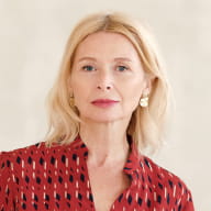 A woman with blonde hair wearing a red patterned blouse poses for a portrait, part of the Perfect.Live team page