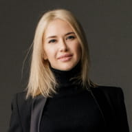A woman with blonde hair wearing a black blazer poses for a portrait, part of the Perfect.Live team page