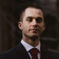 A man in a dark suit and tie poses for a portrait, part of the Perfect.Live team page
