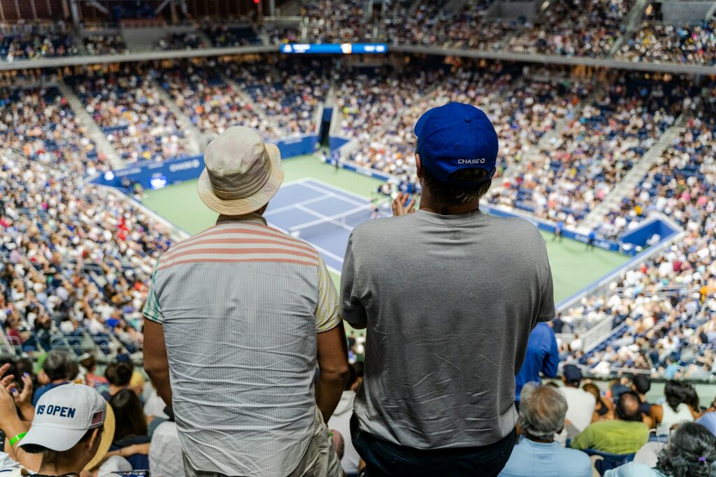 Spectators watching from the upper tier of a packed hard-court tennis stadium