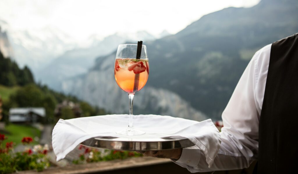 Concierge vs butler comparison — a member of staff presenting a drink at a table set with a mountain view