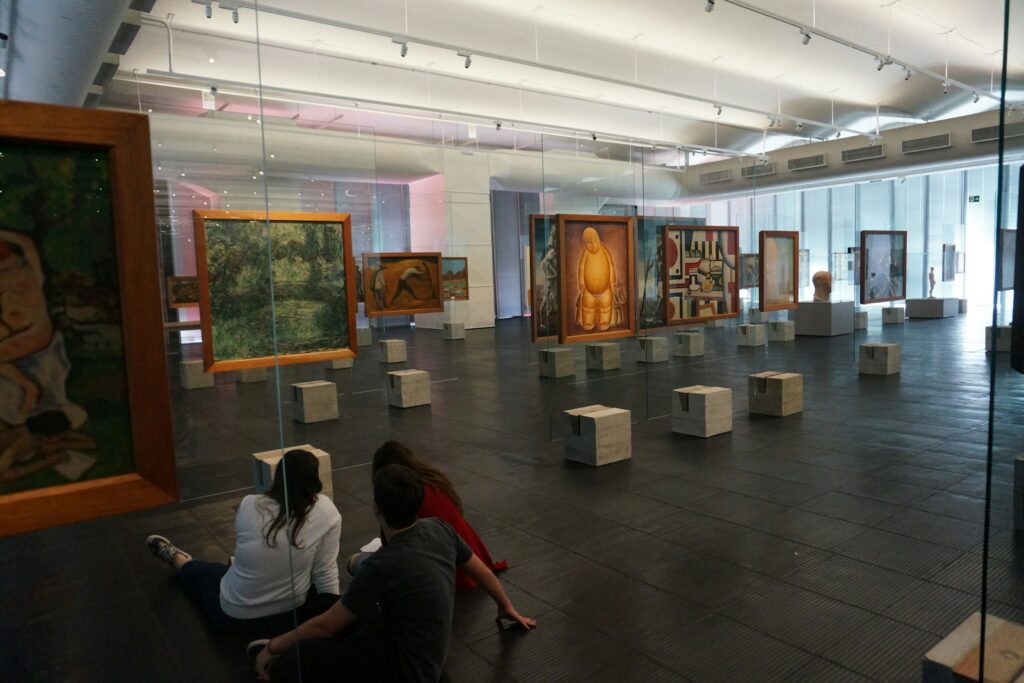 Visitors seated in a gallery looking at paintings on display