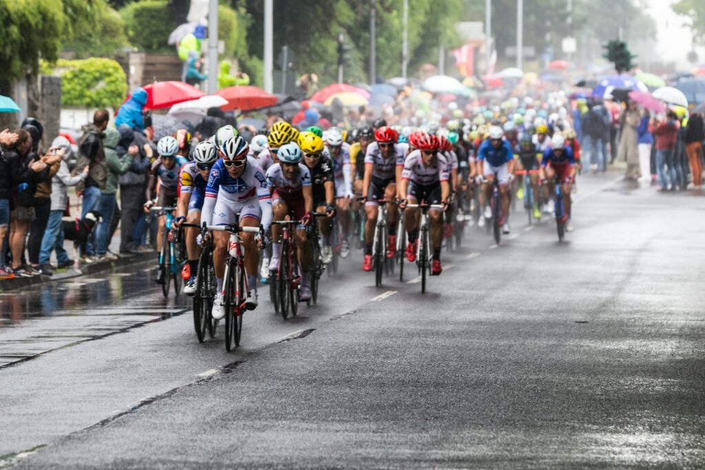 The peloton riding through rain past spectators under umbrellas