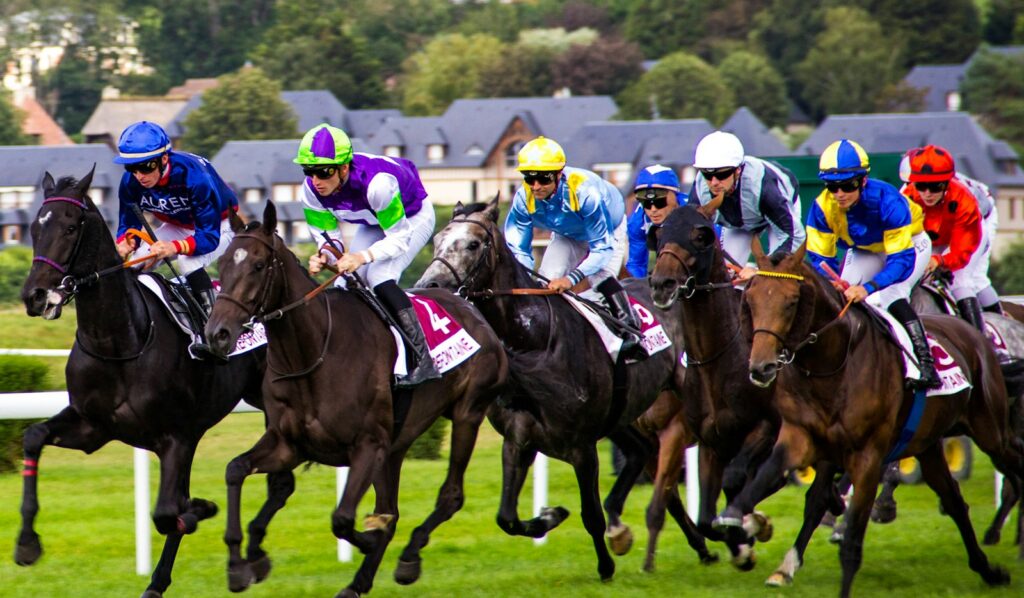 Jockeys in colourful silks driving their mounts down a turf straight in a flat race finish