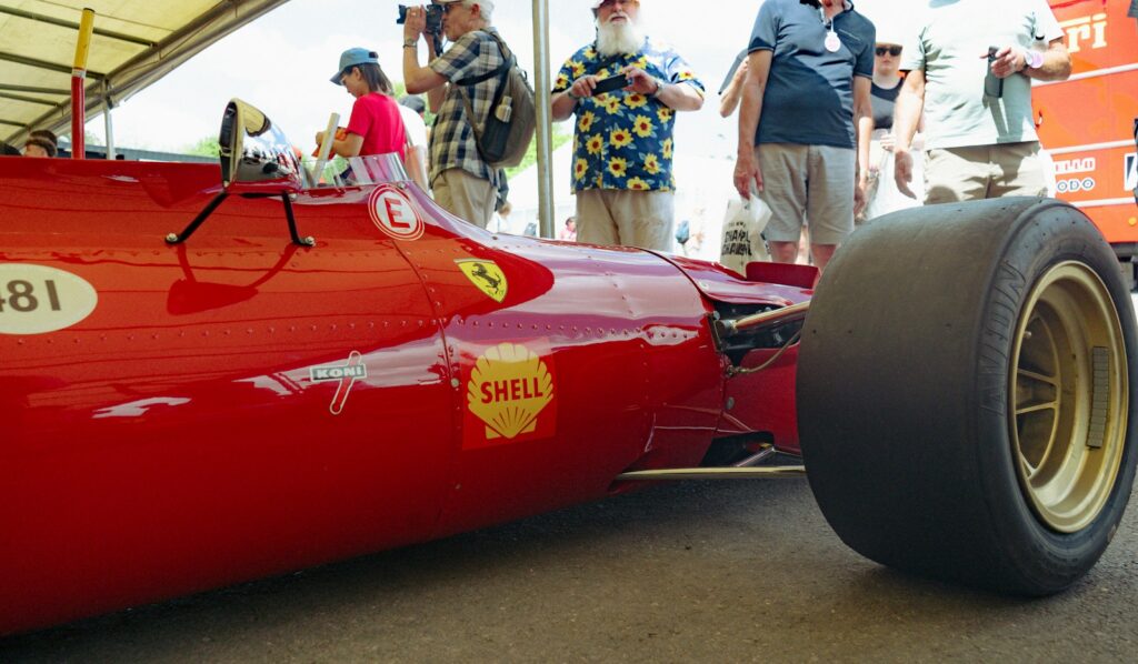 A vintage Ferrari racing car with spectators watching at a historic motor racing meeting