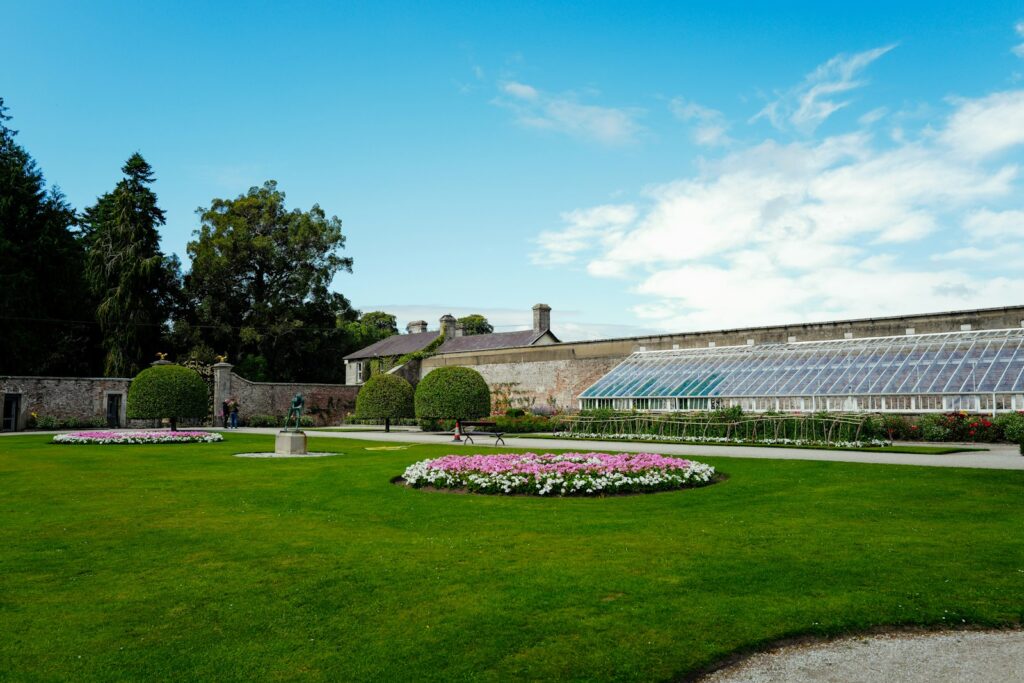 Manicured garden lawn with a glasshouse and historic building in the background