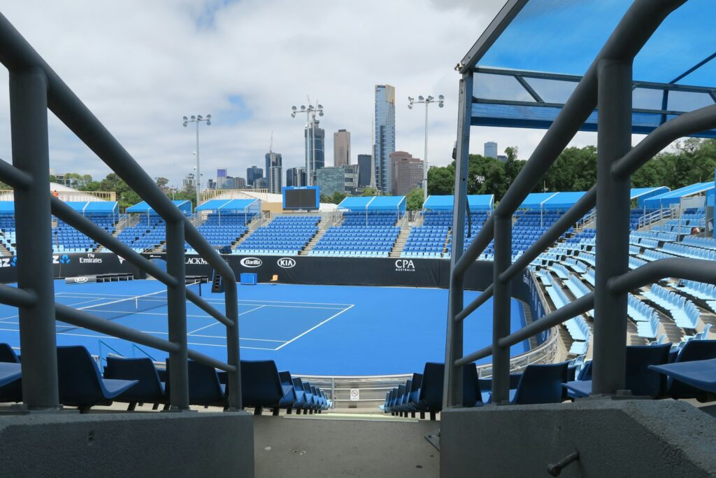 An empty blue hard-court tennis stadium with a city skyline behind it