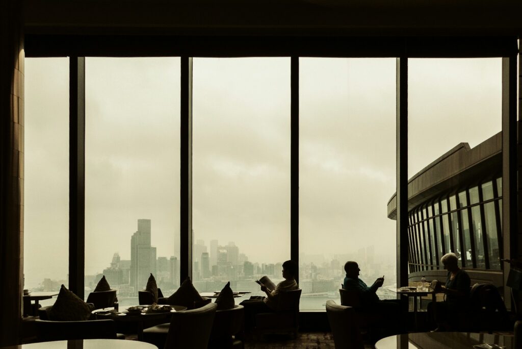 A quiet high-floor lounge at dusk with guests seated at a distance and the city beyond the windows