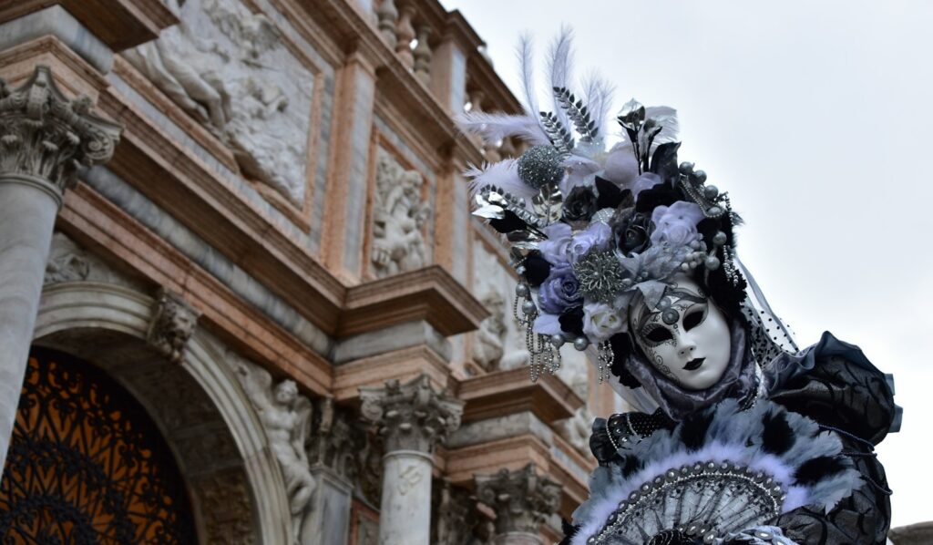 Costumed figure in a mask before a Venetian façade during the Venice Carnival