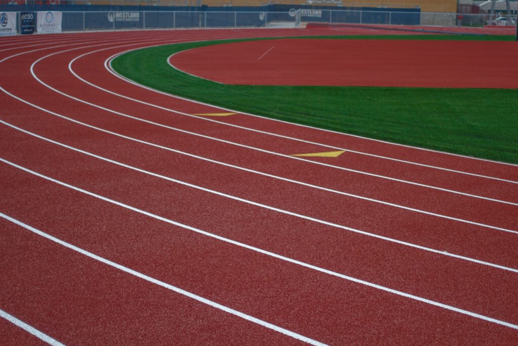 Empty red athletics track curving around a green infield in a stadium