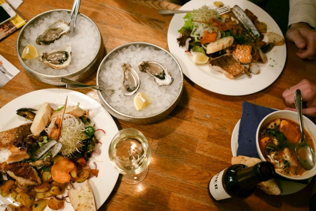 Oysters on ice, grilled fish, and fish stew with a glass of white wine on a restaurant table