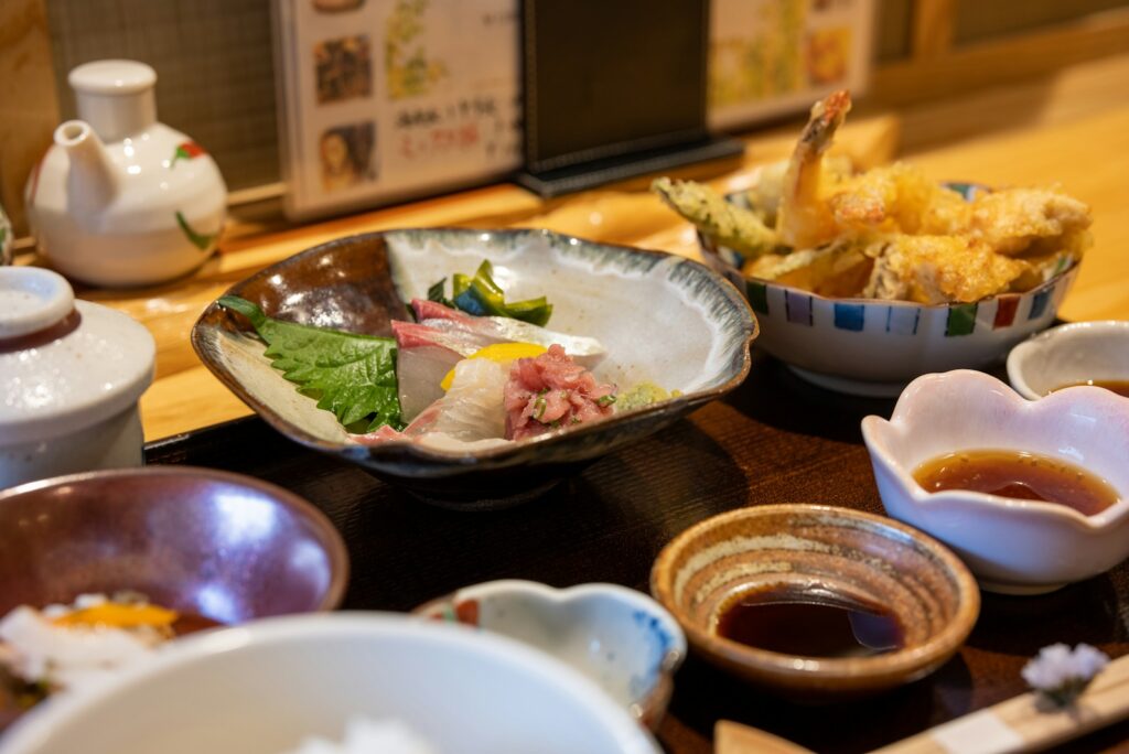 Wooden counter set with small plates of sashimi, tempura, and sauces