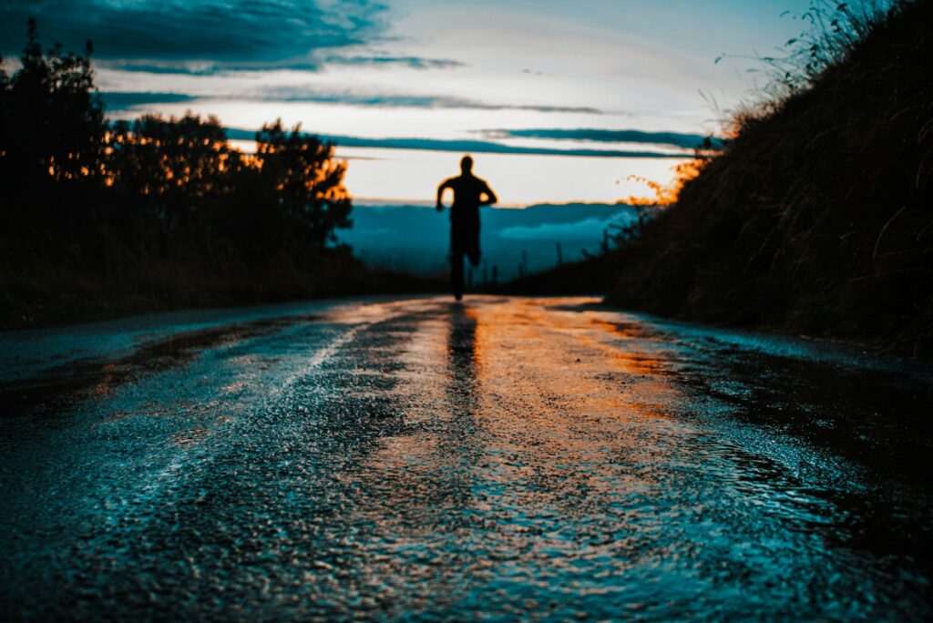 Lone runner in silhouette on a wet country road at dusk