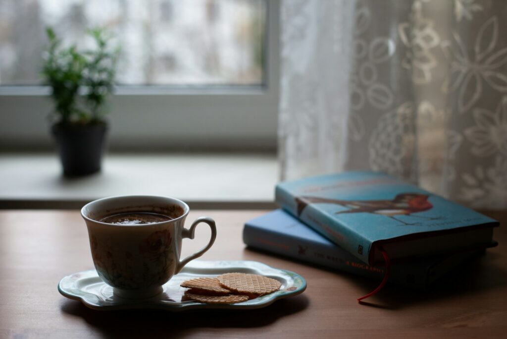 Teacup and books on a sunlit windowsill beside soft lace curtains