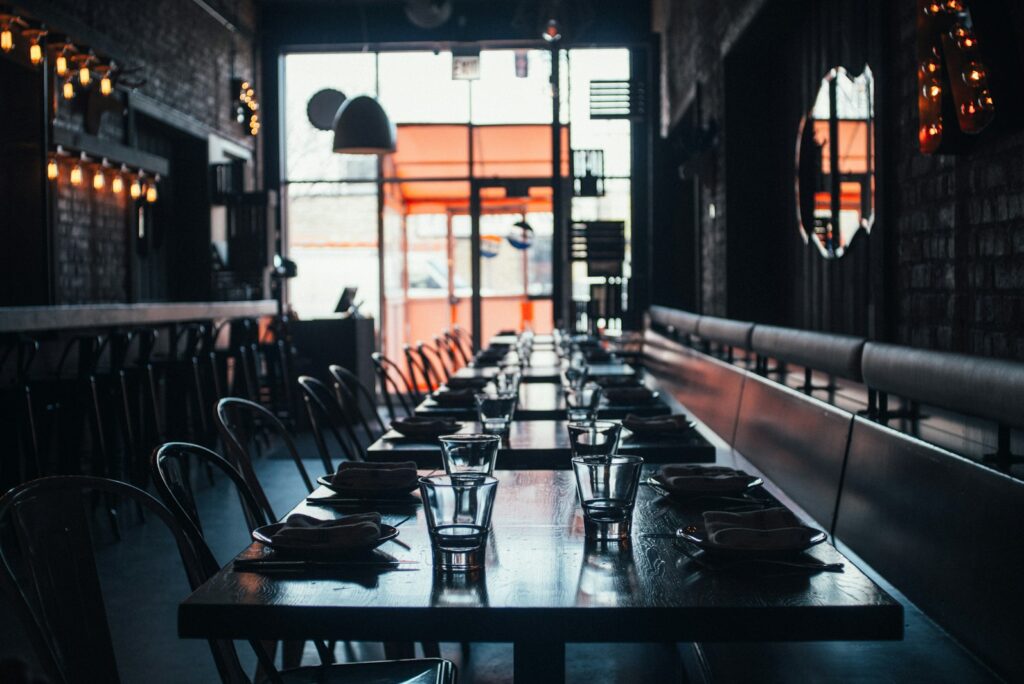 Dimly lit Chicago restaurant interior with a long set table, banquette seating and tall windows