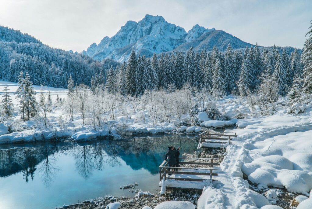 Snow-covered alpine lake with a wooden jetty and two small figures in winter light