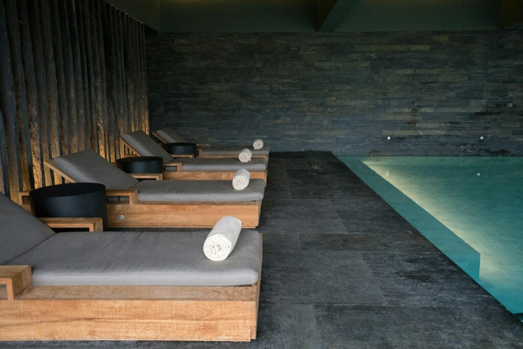 Teak loungers with rolled towels beside a softly lit indoor spa pool