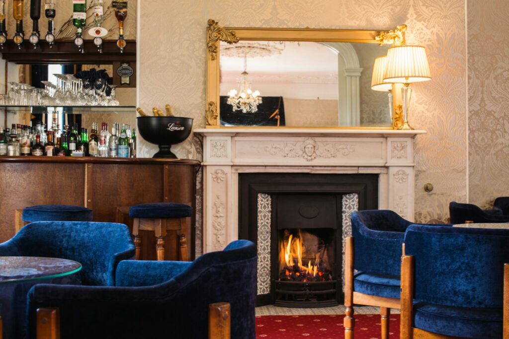 A members club lounge with velvet armchairs around a lit fireplace