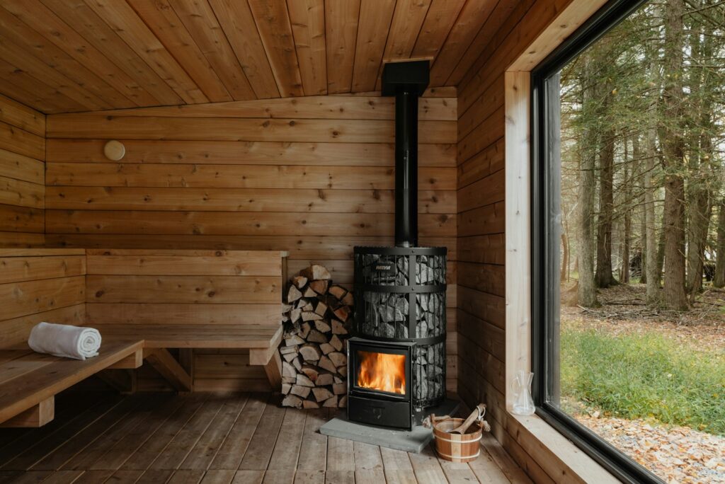 Wooden sauna with a wood-burning stove and a large window onto the forest