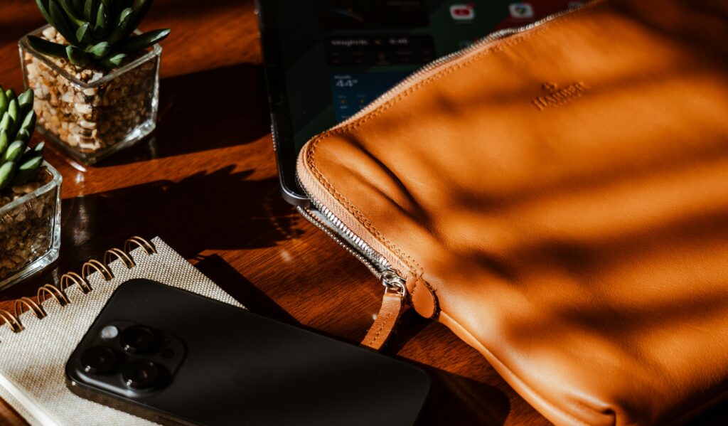 Leather laptop sleeve, notebook, and phone on a sunlit desk, a quiet setting for executive assistant services