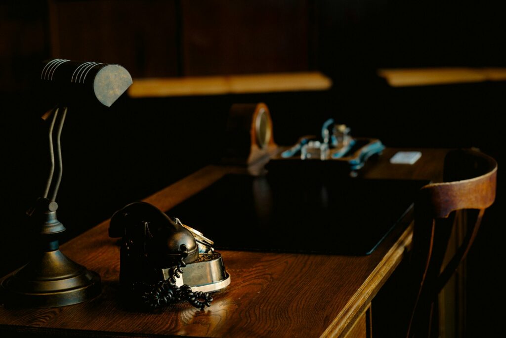 Vintage telephone beside a brass desk lamp on a dark wooden desk.