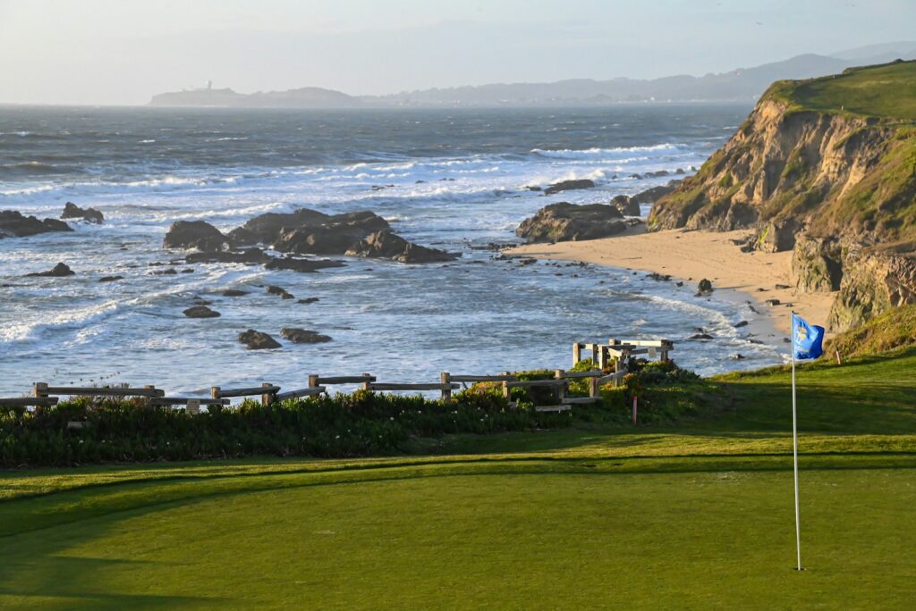 Golf green with a flag above a sandy beach and rocky coast
