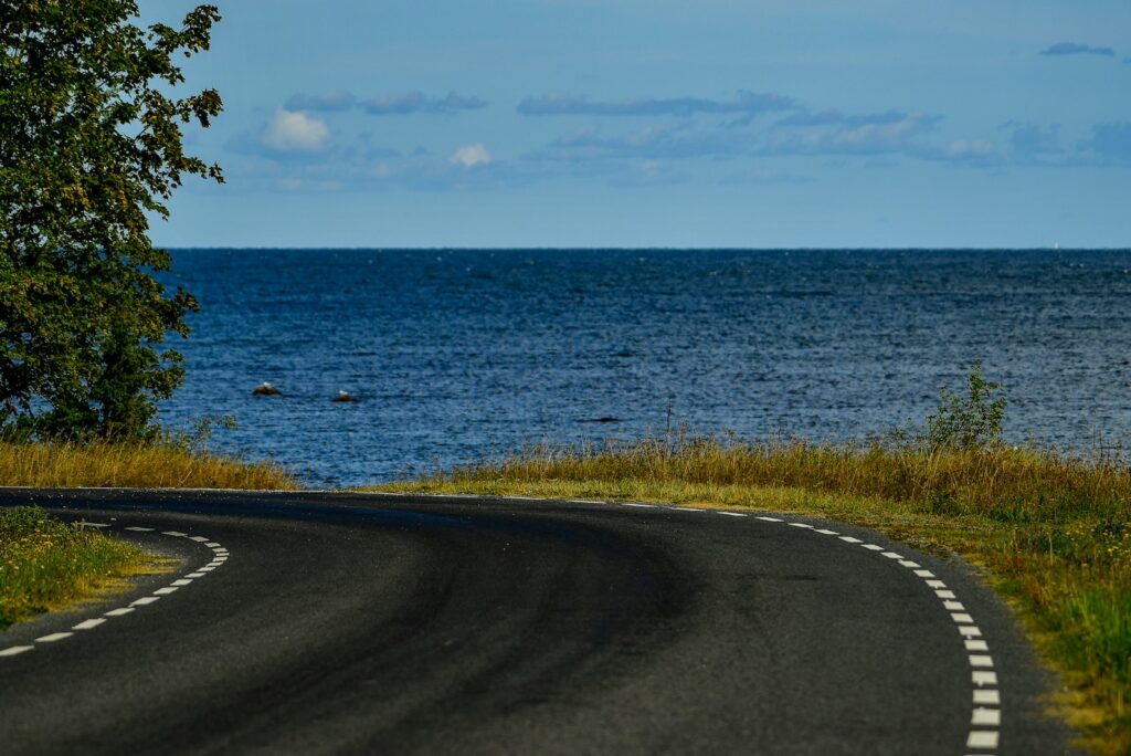 Empty winding coastal road curving towards the open sea under a partly cloudy sky