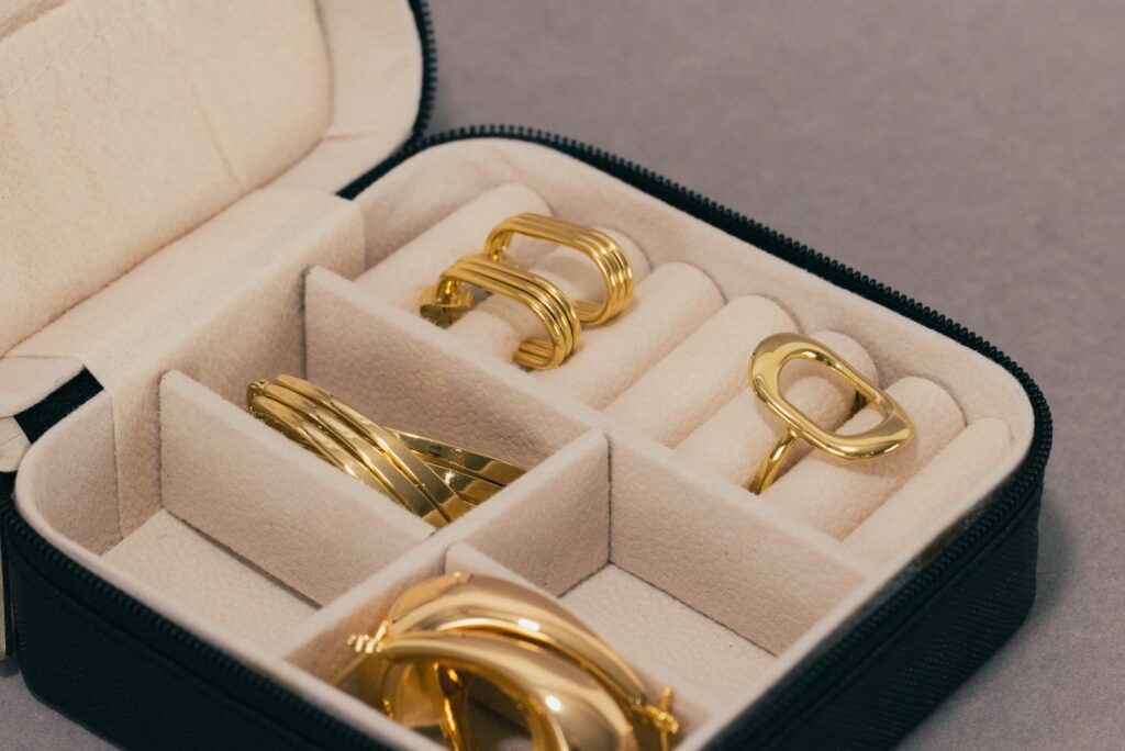 Open jewellery case holding gold rings and earrings on a grey surface.