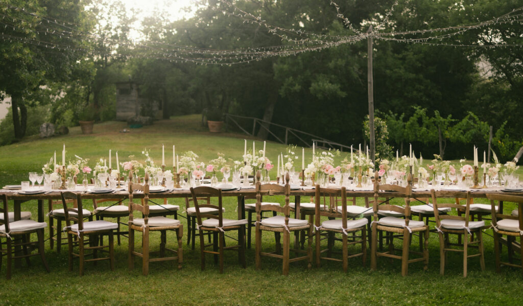 Luxury event planning — long dinner table set with candles and flowers in a private garden at dusk