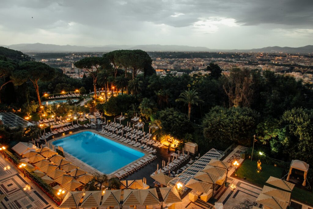 Rome hotel pool and landscaped gardens lit at dusk with the city stretching out below