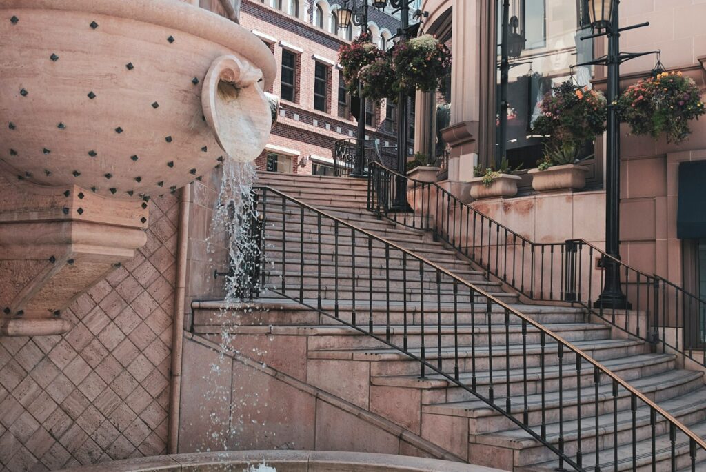 Travertine fountain and stone staircase on a Rodeo Drive shopping lane in Beverly Hills, with hanging flower baskets.