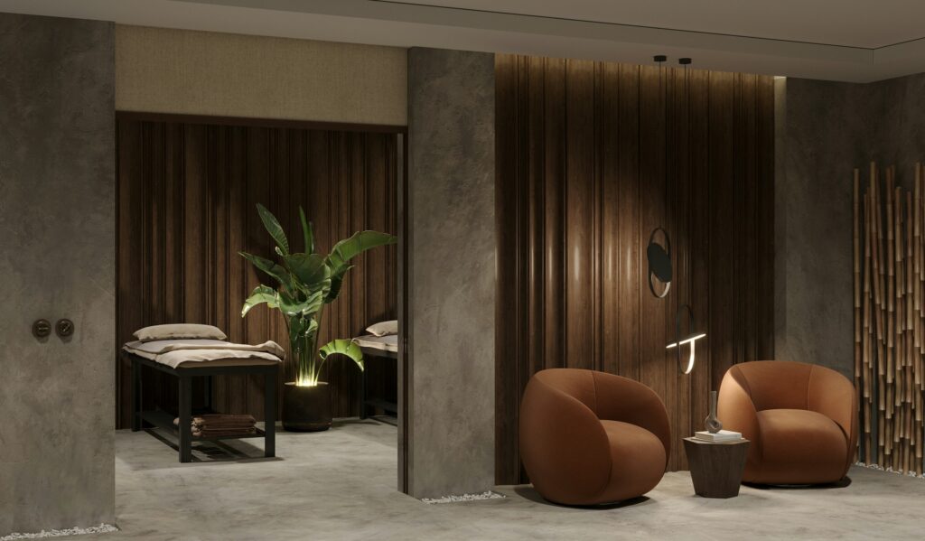 Medical spa treatment area with two couches, a potted plant, and a pair of rounded armchairs in low, warm light