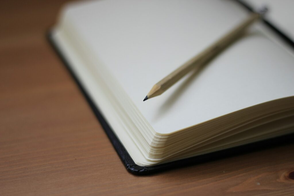 Open notebook with a pencil resting on the page, softly out of focus on a wooden desk