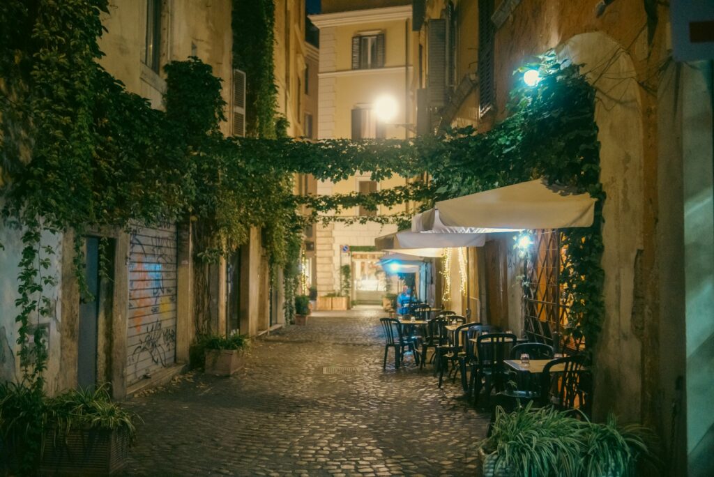 Ivy-draped cobblestone alley in Rome with restaurant tables in the evening