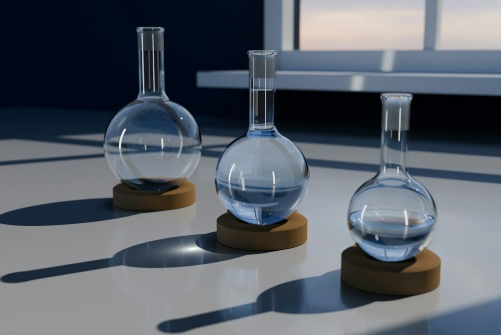 Three clear glass laboratory flasks on cork stands, casting soft shadows on a white surface