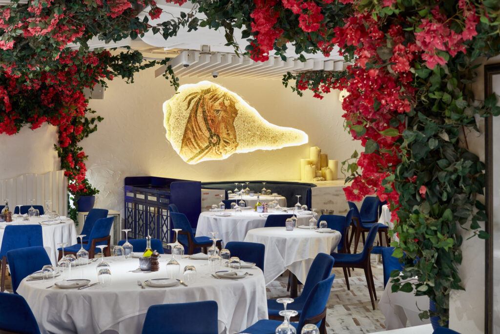 Mosaic horse wall and white-clothed tables beneath bougainvillea at OPA Dubai