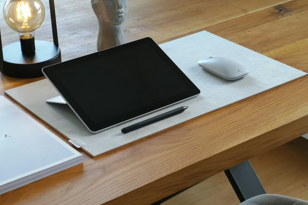 Blank tablet and notebook on an oak desk beside a warm table lamp