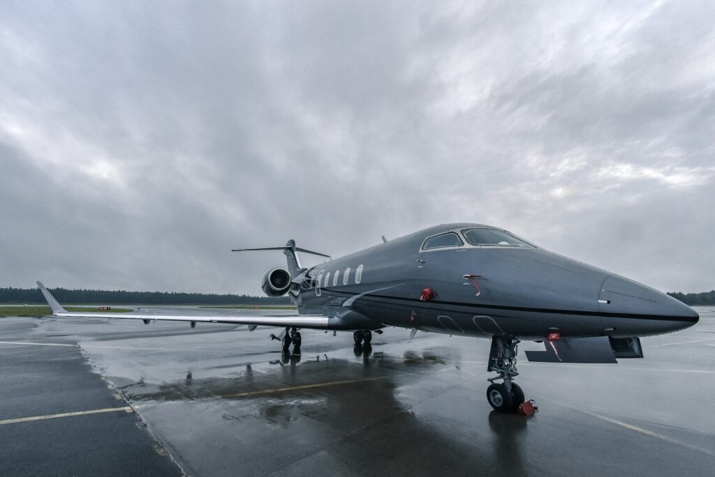 Dark private jet parked on a wet apron under a heavy grey sky