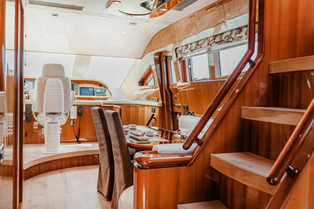 Yacht salon with a helm station, a polished wood dining table, and a staircase to the upper deck