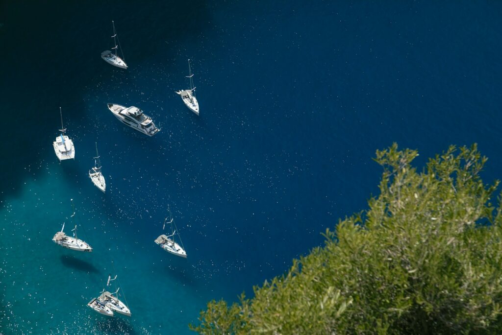 Yachts at anchor in a deep blue bay seen from the cliffs above