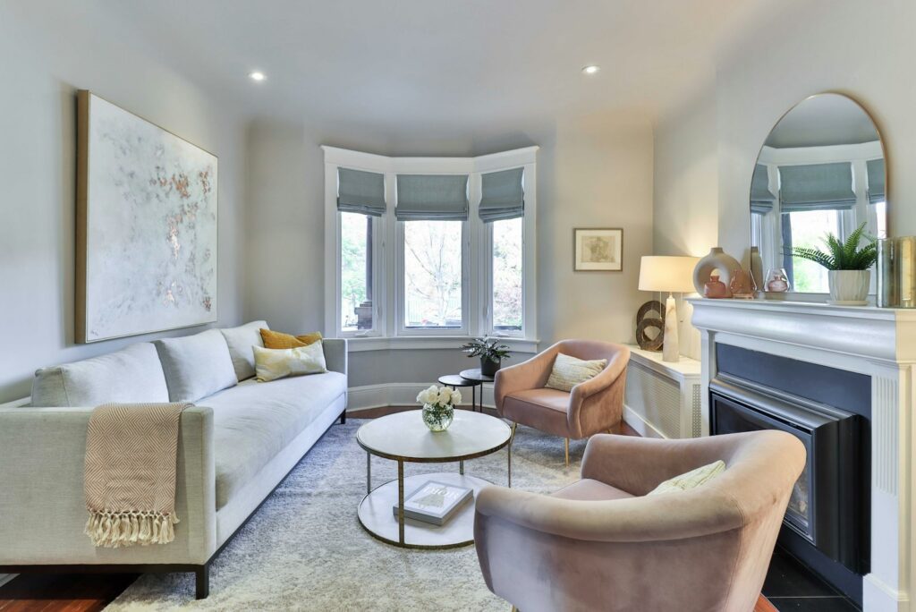 A bright living room with a pale sofa, blush armchairs, and a bay window