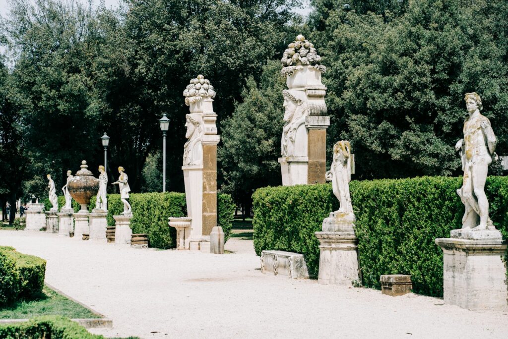 A path lined with stone statues and clipped hedges in a Roman park