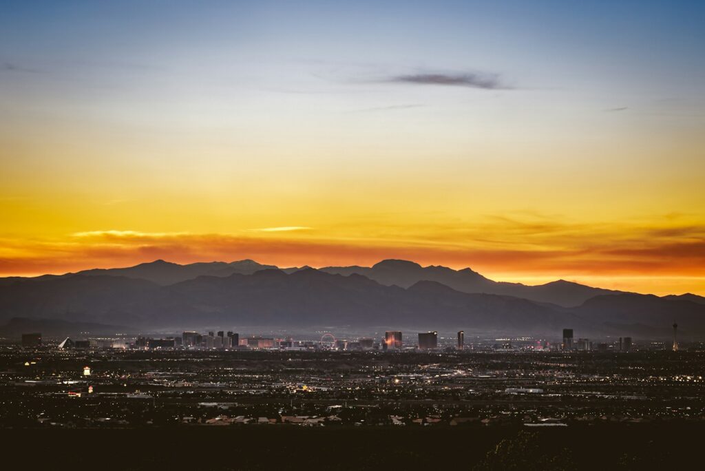 Las Vegas skyline and observation wheel at dusk beneath a golden sunset over the mountains
