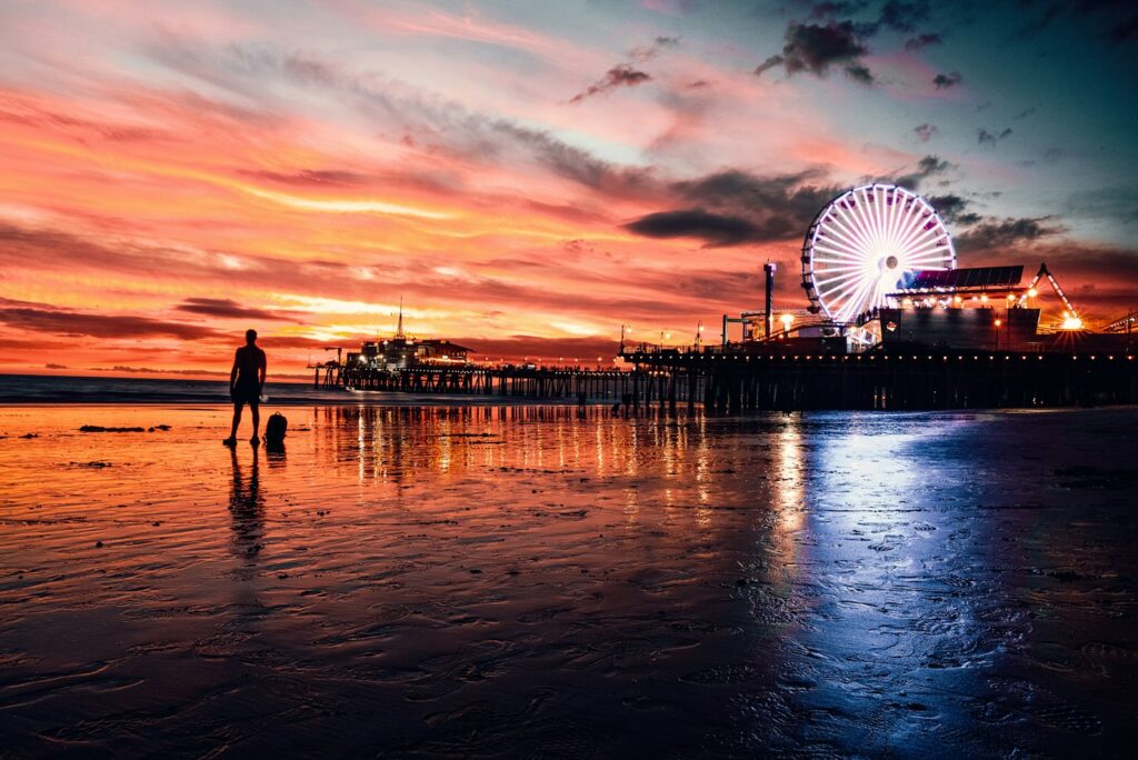 Santa Monica Pier and its Ferris wheel under a red sunset sky, reflected on the wet sand