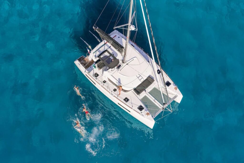 Aerial view of a white catamaran at anchor in clear blue water with guests swimming beside it
