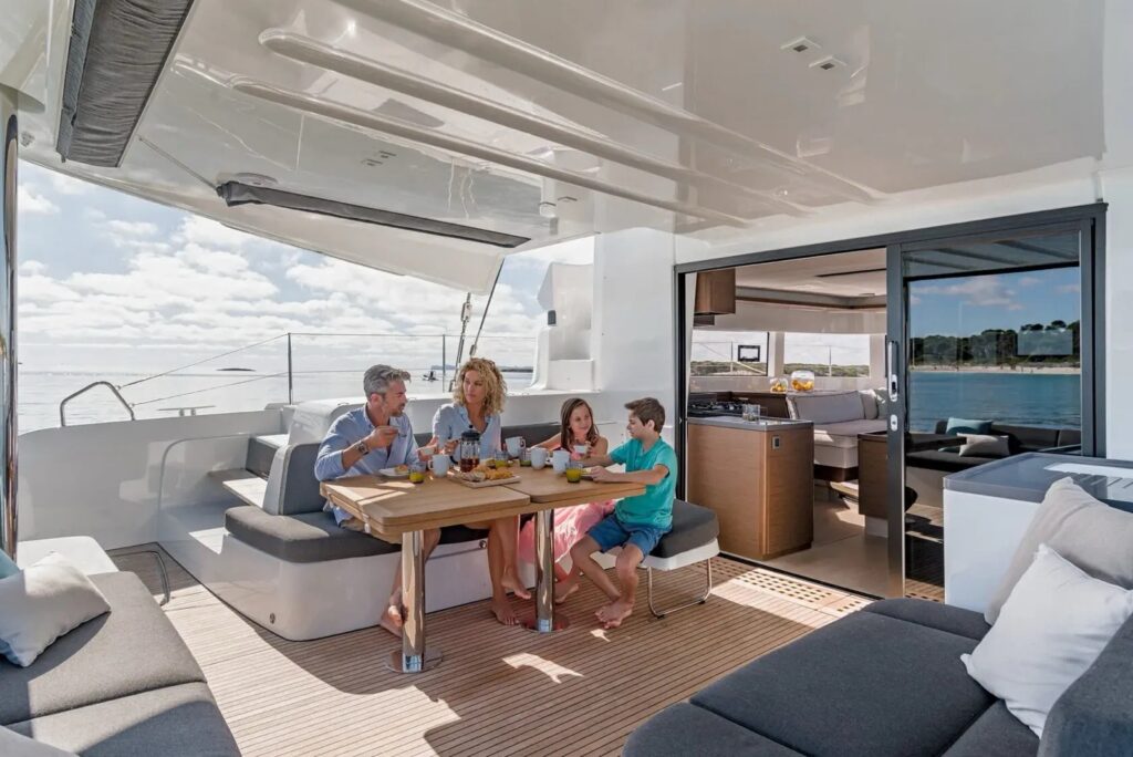 Family having breakfast at the table in the shaded cockpit of a catamaran