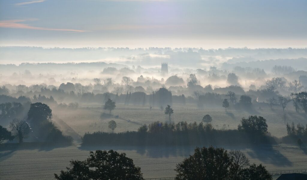 Wellness retreat UK: misty Cotswolds countryside at sunrise, with a church tower rising above the valley