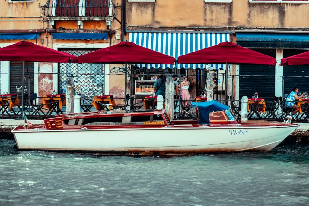 Wooden water taxi moored beside a canal-side restaurant terrace in Venice