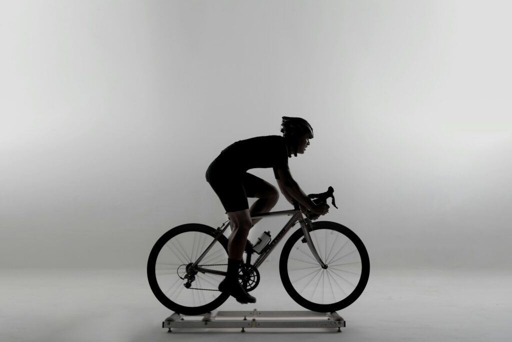 Silhouette of a cyclist riding a road bike on a stationary trainer against a pale studio backdrop
